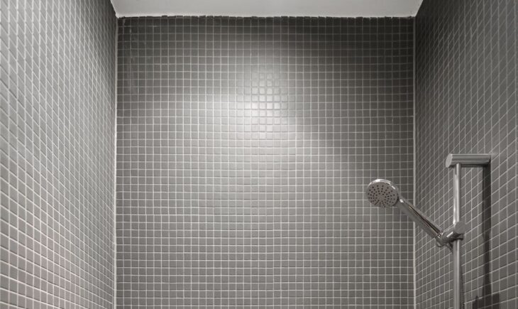 Walk-in shower lined with small matte grey mosaic tiles, with a chrome handheld shower head on a slide rail